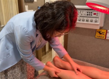 원장이 환자의 종아리와 발뒤꿈치 위 아킬레스건염 부위를 손으로 눌러 확인하는 뒤쪽 모습